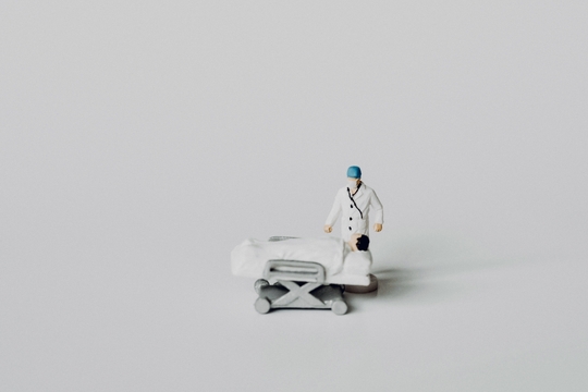 Foto van miniatuurfiguurtjes: een verpleegkunde of dokter staat naast een patient op een ziekenhuisbed.