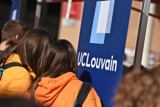 Studenten bij een banner van UCLouvain.