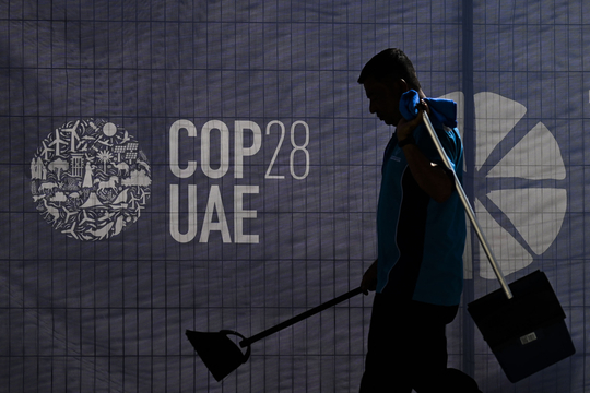 Een onderhoudsmedewerker wandelt voorbij een scherm met het logo van COP28 in de Verenigde Arabische Emiraten.