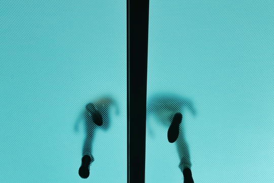 Een foto van onderuit van twee personen die op een glasoppervlak lopen.