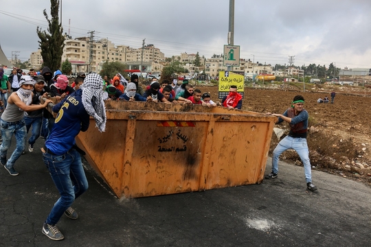 Jongeren verplaatsen een container die bescherming moeten bieden tegen de Israelische soldaten, tijdens clashes in Albireh/Ramallah, bij de Israelische kolonie Beit El. (Foto Muhanned Darabee)